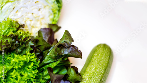 Still life of fresh, green vegetables. Zucchini, young cabbage, lettuce. On a gray background. It is located on the left. Space for text. Vertical photo. The view from the top