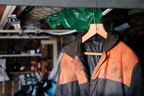 Dirty warm overalls, work clothes on a wooden hanger in the pantry.