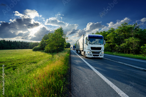 Obraz na płótnie White truck driving on the asphalt road between the forest and the clearing at sunset w salonie