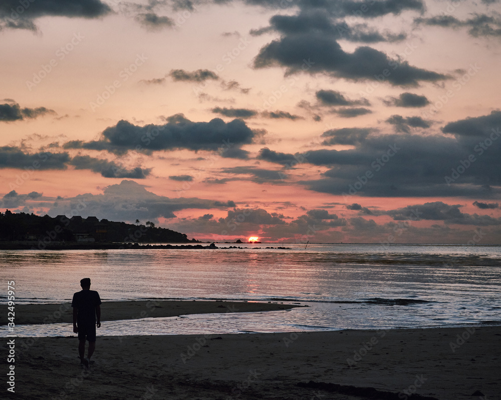 Man walking on the beach at sunrise with dramatic clouds in Thailand. Ko Yao Noi island.