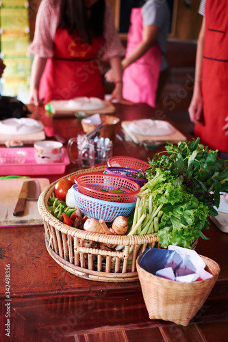 Vegetable preparation during cooking class in Thailand Chiang Mai. The wooden table full of ingredients. Cooks in the background.