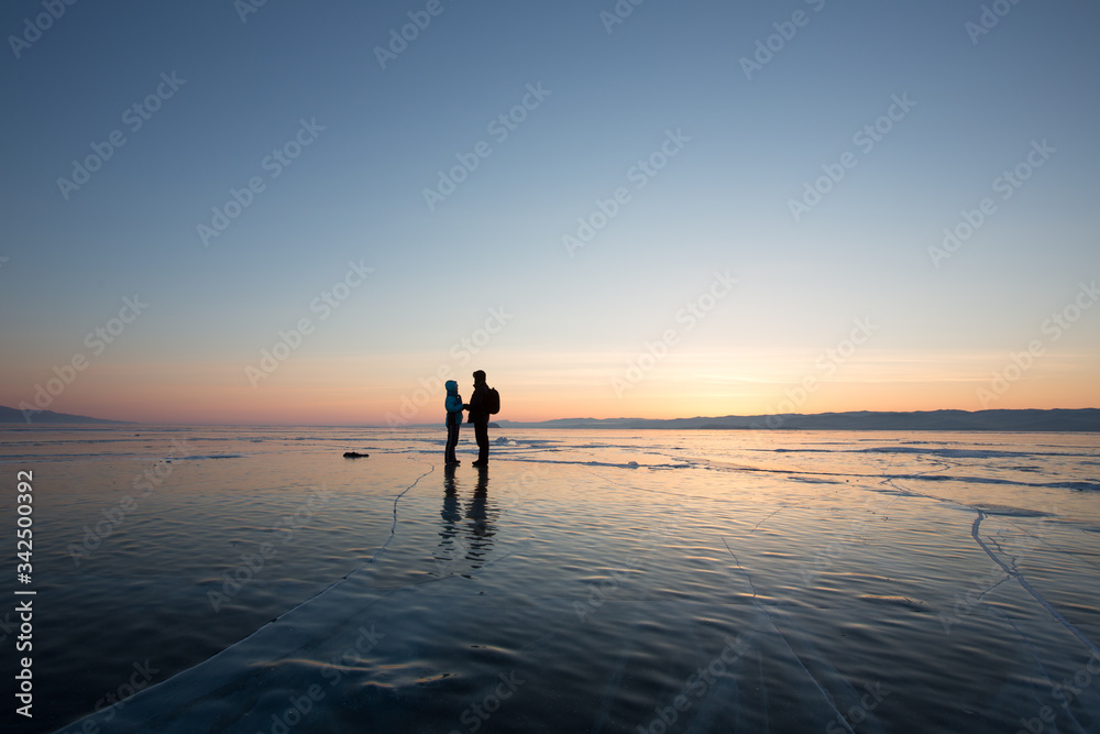 A guy and a girl are facing each other holding hands on the ice of Lake Baikal in the rays of dawn