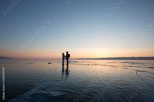 A guy and a girl are facing each other holding hands on the ice of Lake Baikal in the rays of dawn