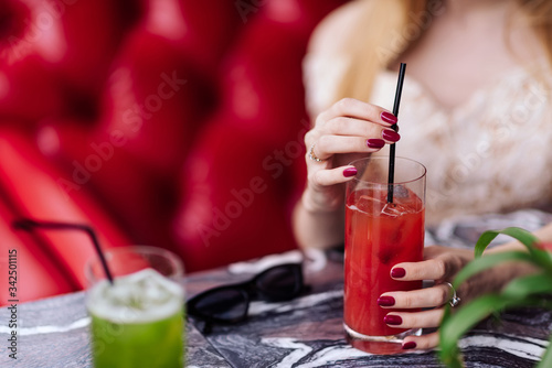a girl in a beige dress drinks red juice in a restaurant on a red sofa