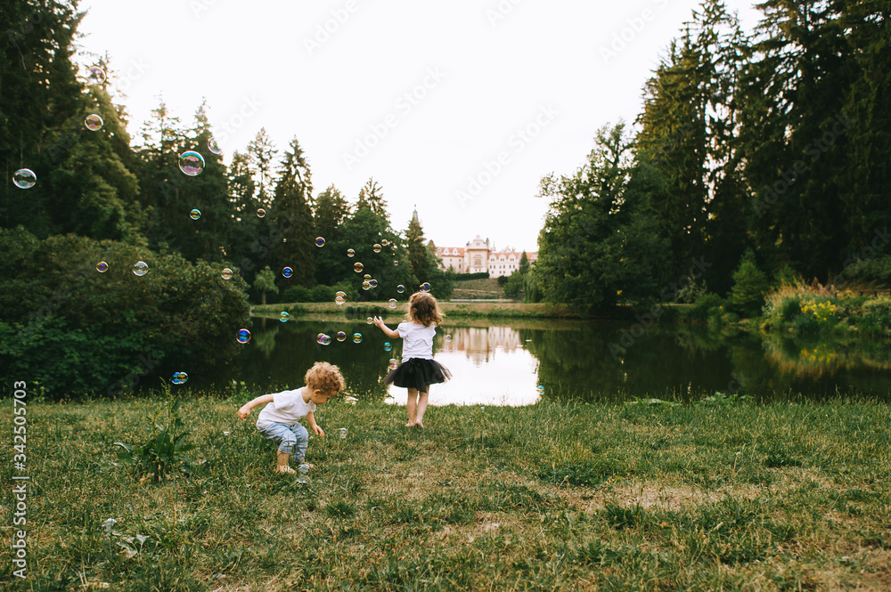 Two cute little children playing with bubles near the lake in sunny summer