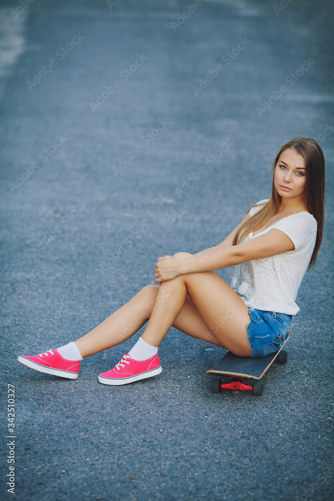 A young girl in short shorts sitting on a skateboard. Stock Photo