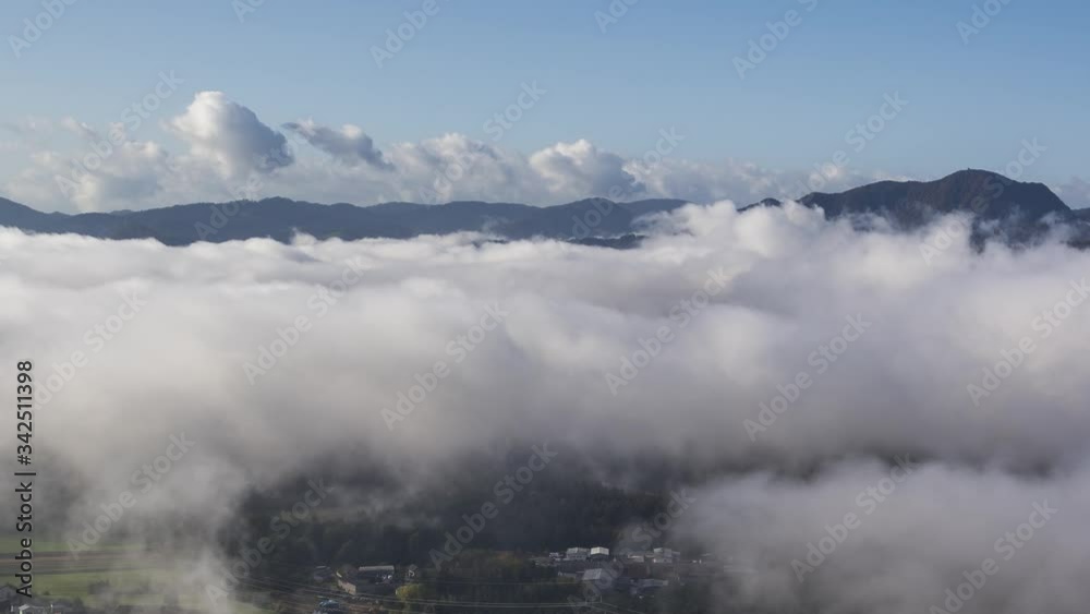 Zoom in time lapse low inversion clouds rolling over valley, View of mountains in distance. Bellow small village and forest, Slovenia Zoom in time lapse low inversion clouds rolling over valley, View of mountains in distance. Bellow small village and forest, Slovenia