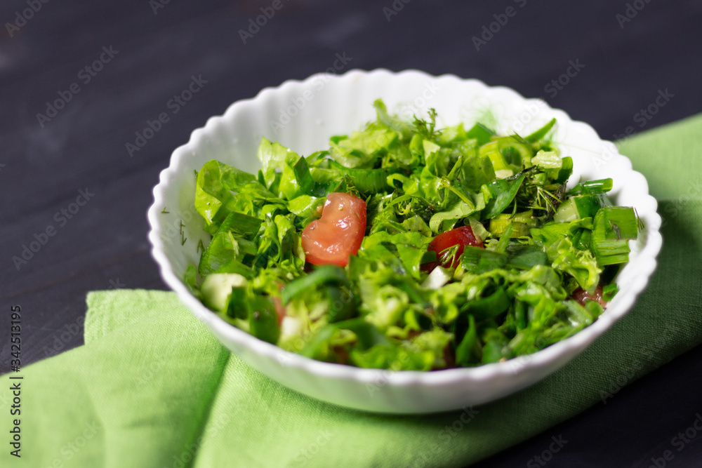 salad with arugula, cucumber, greenery and tomatoes in white bowl on green textile on black wooden background salad with arugula, cucumber, greenery and tomatoes in white bowl on green textile on black wooden background
