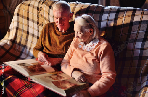 two elderly people-a man and a woman looking at a family photo album smile and hug each other wrapped in a warm plaid blanket.