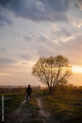 Girl in jacket and cap riding bicycle into susnet
