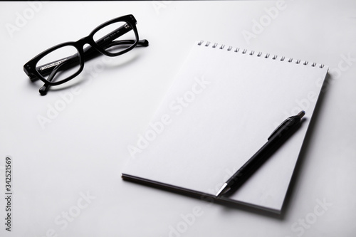 White notebook and black glasses on light background