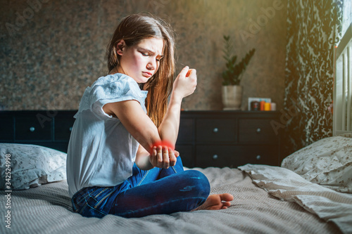 Tableau sur toile young brunette girl sits on a bed in her room, holds a sore elbow with her hand