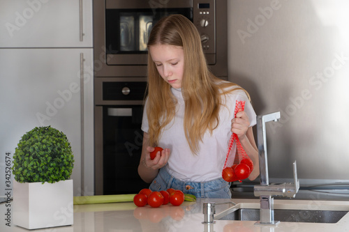 a girl with long blond hair holds tomatoes in her hands to wash them at the kitchen sink
