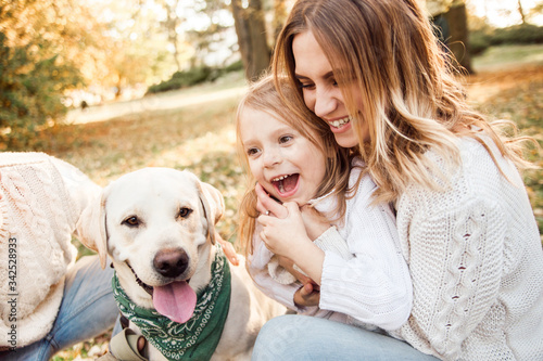 Happy beautiful family with dog labrador is having fun  are sitting on green grass in park. © zadorozhna