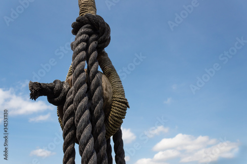 Vintage block and tackle with elaborate knots and wrapping on an old sailing vessel against a blue sky with clouds, horizontal aspect