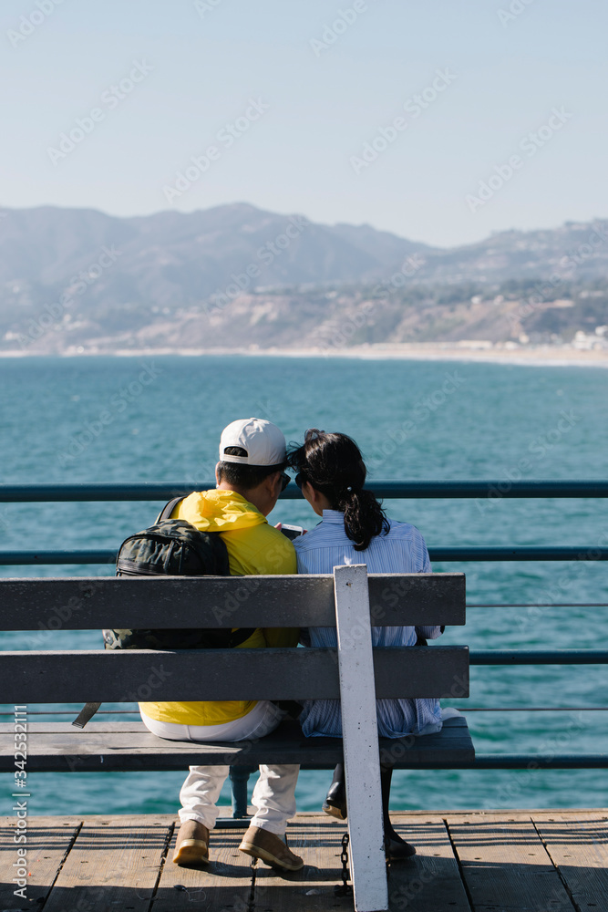 Asian couple hugging and staring at the blue ocean in santa monica pier, california, during sunset hours in the summer