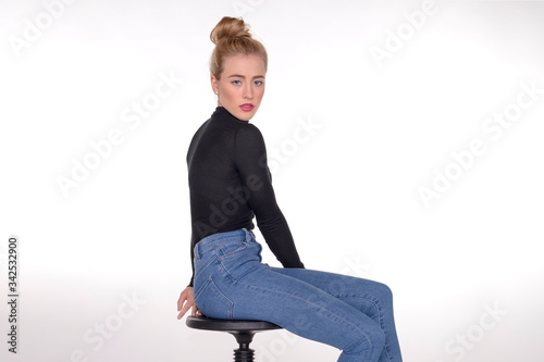 Pretty teen girl in skinny jeans and black sweater seated on stool.
