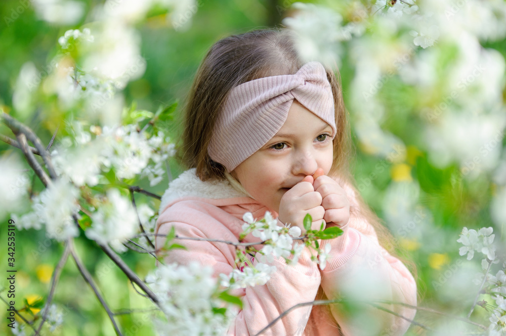 Beautiful little girl portrait near a blossoming cherry tree. The child smiling on green natural background Beautiful little girl portrait near a blossoming cherry tree. The child smiling on green natural background