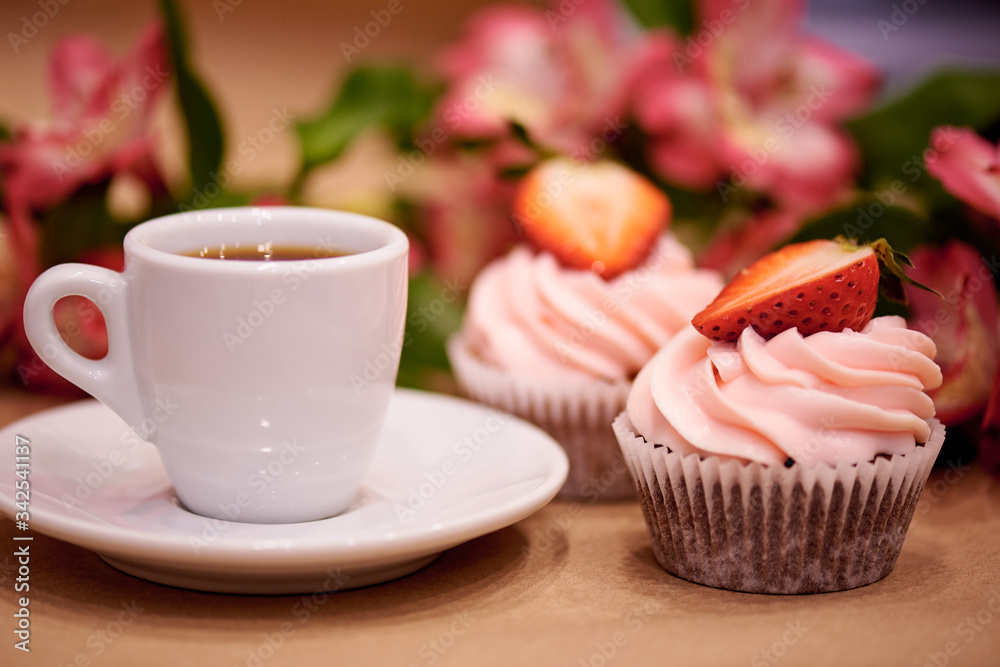 Chocolate cupcakes with strawberries. Cupcakes and a cup of coffee on the table with flowers. Selective focus. Chocolate cupcakes with strawberries. Cupcakes and a cup of coffee on the table with flowers. Selective focus.