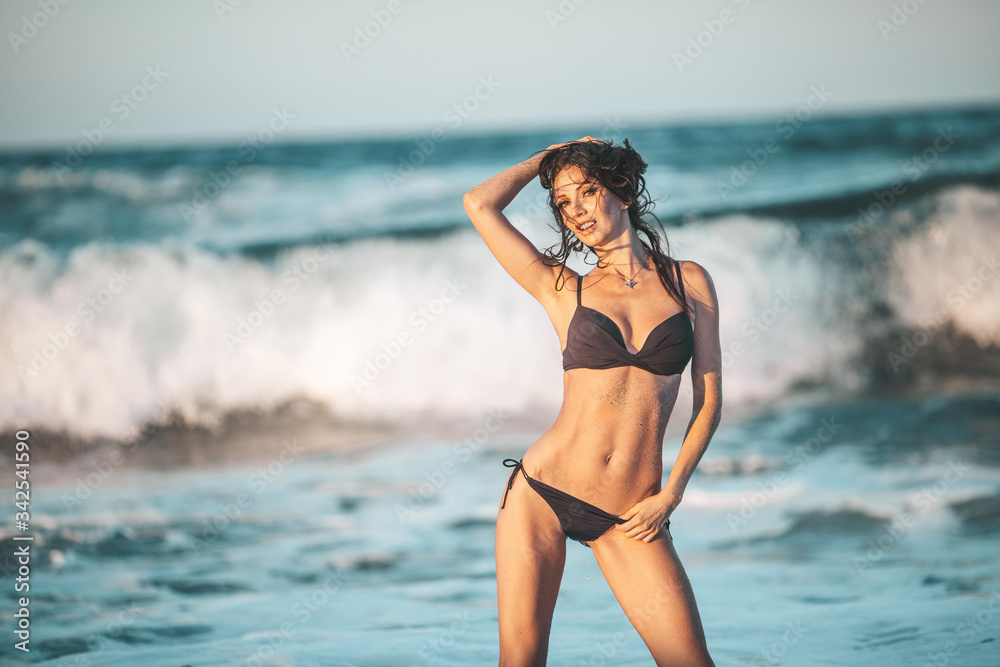 beautiful woman in a black swimsuit in the ocean, a young slender woman stands on a background of waves