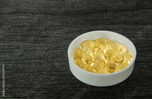 Yellow soft shell D-vitamin capsule in bowl. Fish oil capsules with omega 3 and vitamin D on dark wooden background, healthy diet concept. Pills and capsules. Multivitamins and supplement concept.