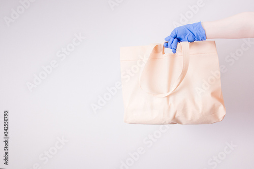 a hand in a blue disposable medical rubber glove holds a shopping bag for shopping, light background, copy space, contactless delivery concept, self-isolation and quarantine, light background.