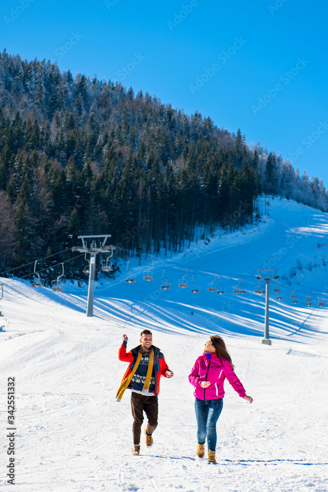 Snowball fight. Winter couple having fun playing in snow outdoors. Young joyful happy multi-racial couple.