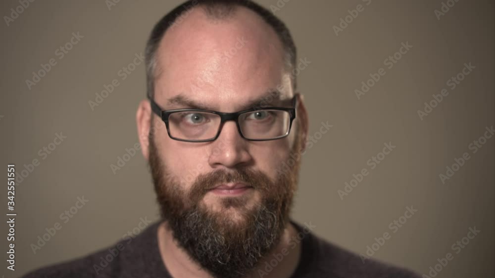 Close up portrait of man with beard and glasses thinking hard or confused about a choice, deep in thought working on a difficult problem to decide. Close up portrait of man with beard and glasses thinking hard or confused about a choice, deep in thought working on a difficult problem to decide.
