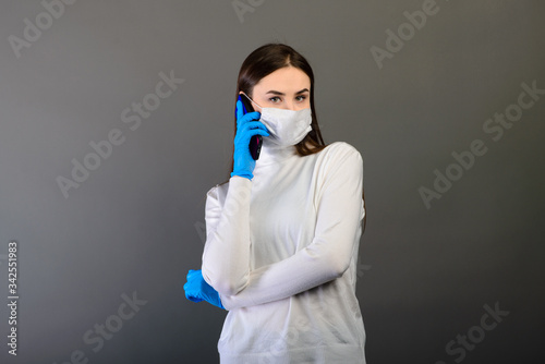 Girl in medical gloves dress a medical mask on her face on a background. Respiratory disease. Covid-19 © Ivan Zelenin
