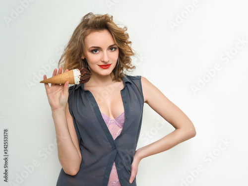 Sexy woman with red lips curly hair in blue blouse and lilac body playfully posing with delicious ice cream on white background looking into camera