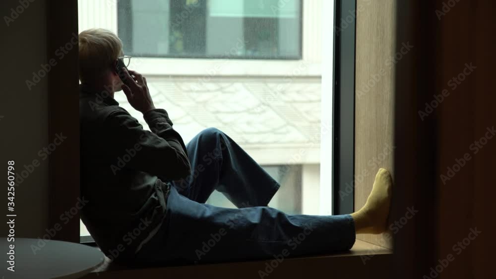 Sad young man looks through window. Stop COVID-19 infection. Touch phone Sad young man looks through window. Stop COVID-19 infection. Touch phone