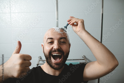 bald happy confused excited young man with beard shaving himself in the bathroom at home