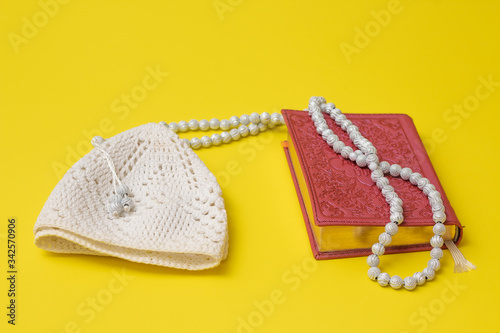 Pink Quran and white muslim rosary and white skullcap on a yellow background