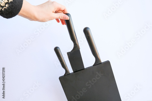 A hand pulling out a knife from a knife stand. Three black knives of different sizes. photo