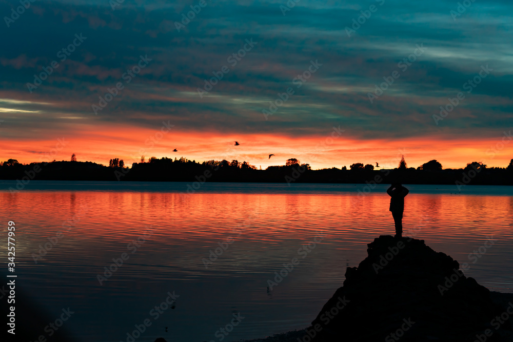 Vibrant sunrise across bay with with silhouette of  figure of person