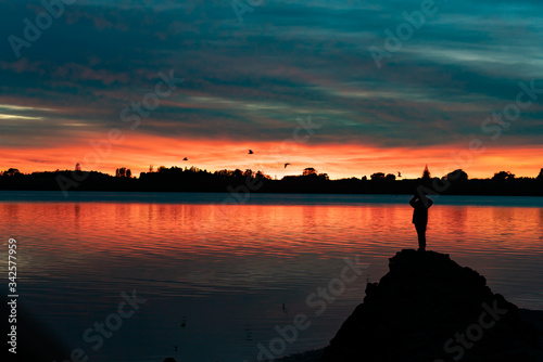 Vibrant sunrise across bay with with silhouette of figure of person
