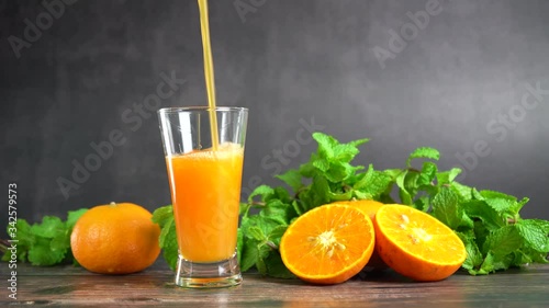 Pouring fresh orange juice into a glass with oranges fruit and peppermint on table, Healthy food.