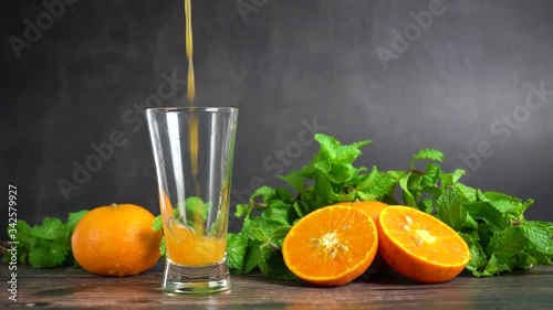 Pouring fresh orange juice into a glass with oranges fruit and peppermint on table, Healthy food. Slow motion.