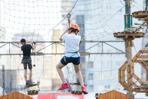 Sporty, young, cute boy in blue t shirt spends his time in adventure rope park in helmet and safe equipment in the park in the summer. Active lifestyle concept