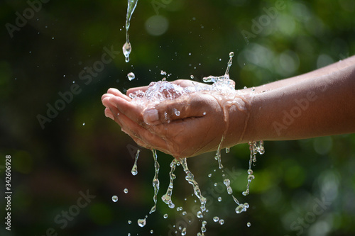Water pouring in kid two hand on nature background. Hands with water splash.