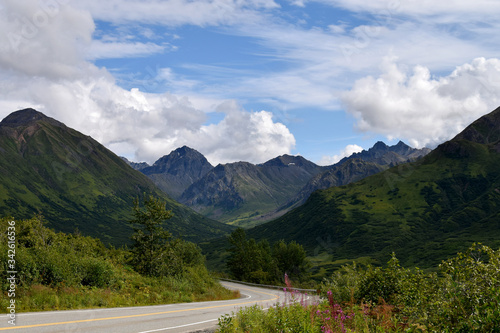 Curving road in Alaska mountains with blue sky and clouds