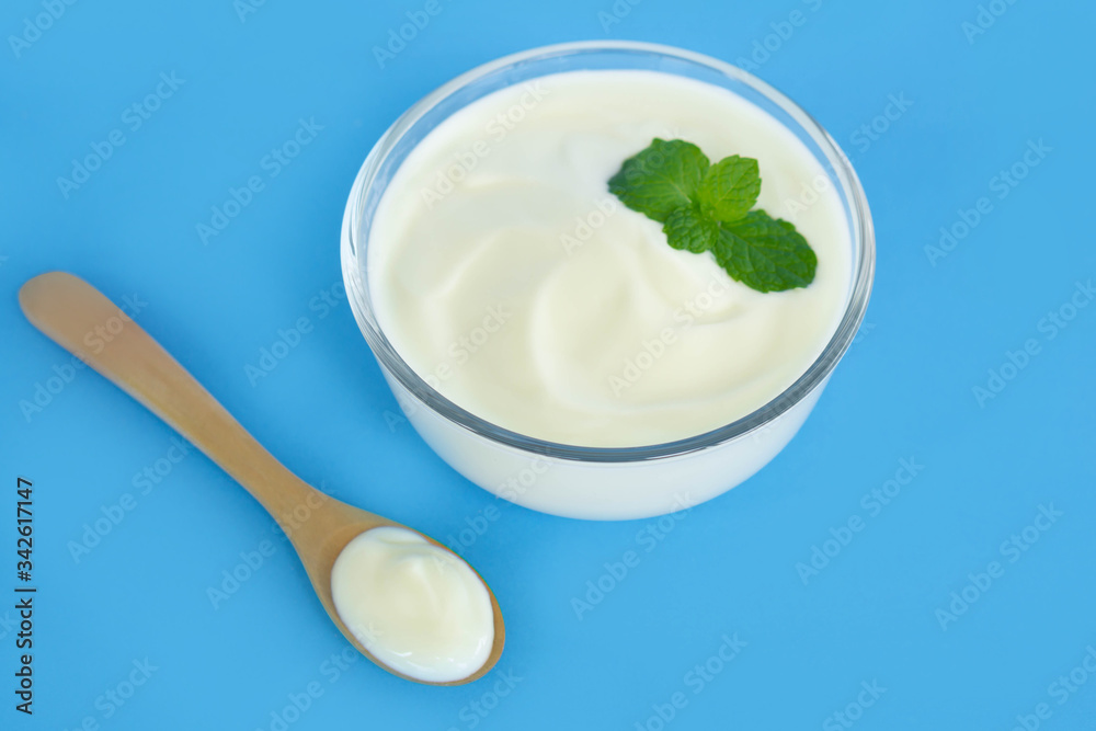 Close up yogurt in glass bowl with wooden spoon on blue background Close up yogurt in glass bowl with wooden spoon on blue background