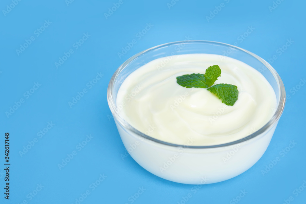 Close up yogurt in glass bowl with wooden spoon on blue background Close up yogurt in glass bowl with wooden spoon on blue background