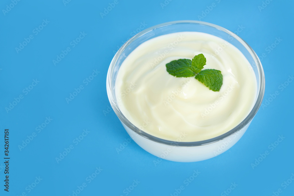 Close up yogurt in glass bowl with wooden spoon on blue background Close up yogurt in glass bowl with wooden spoon on blue background