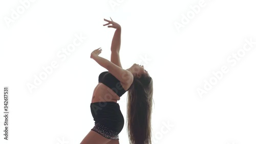 Medium long shot of young beautiful woman with long hair and a beautiful plump figure in a black top and a short black skirt dances belly dance, oriental dance on a white background,  isolated