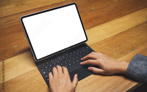 Mockup image of a hands using and typing on tablet keyboard with blank white desktop screen as computer pc on wooden table