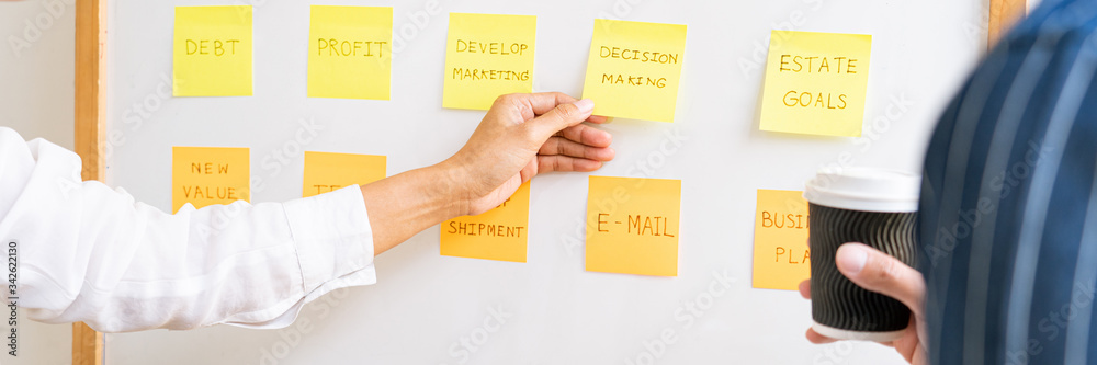 Business people arranging sticky notes commenting and brainstorming on work priorities colleague in a modern co-working space.