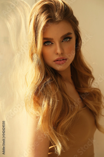 beautiful young woman with blond natural hair and light makeup posing at studio