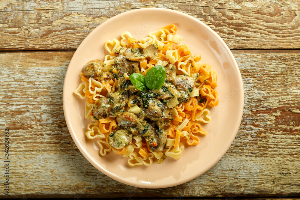 Pasta with mushrooms in a creamy sauce with spinach on a wooden table. Pasta with mushrooms in a creamy sauce with spinach on a wooden table.