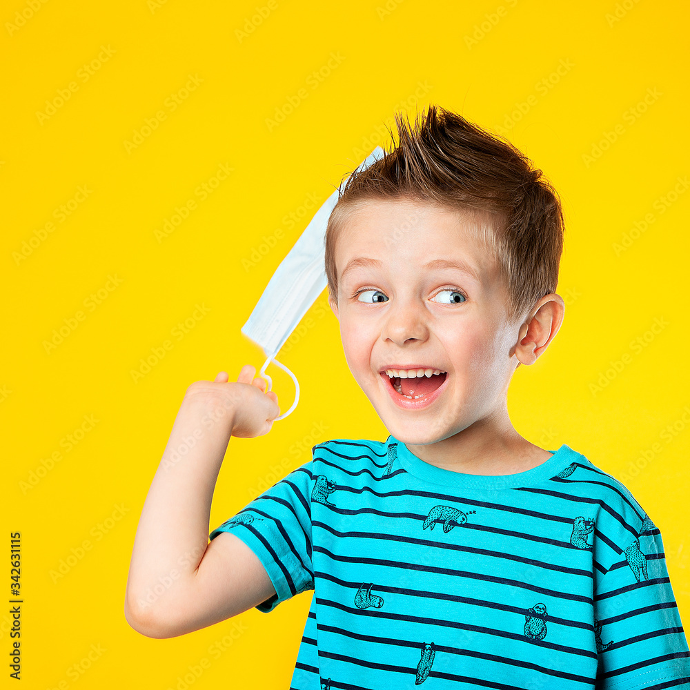 A five-year-old child is happy, waving a medical mask in connection with the end of the pandemic. The end of the coronavirus epidemic. The boy laughs, is happy, and smiles. On yellow background. A five-year-old child is happy, waving a medical mask in connection with the end of the pandemic. The end of the coronavirus epidemic. The boy laughs, is happy, and smiles. On yellow background.